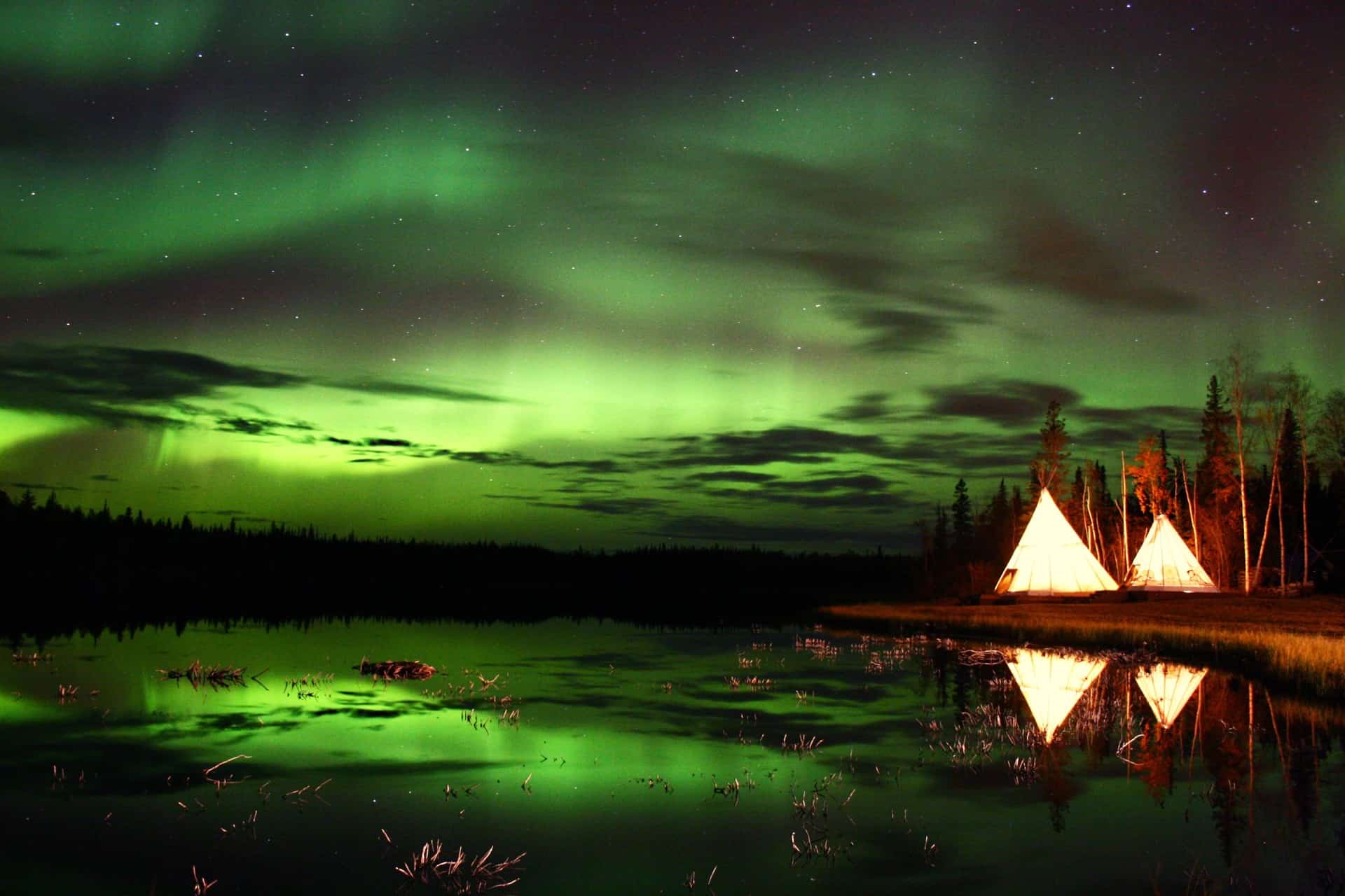 https://www.discovercanadatours.com/wp-content/uploads/2022/05/Aurora-Village-Yellowknife-Northwest-Territories-Canada-Aurora-Borealis-Northern-Lights-Summer-Two-Teepees-Reflection-Landscape-Colourful-perfect-Green-Hero.jpeg